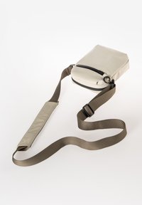 Borsa a tracolla grigia chiara con forma arrotondata, zip superiore e tracolla regolabile di colore verde oliva. Presenta un esterno testurizzato e un design minimale.
