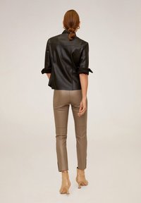 Musta tekonahkatakki, jossa on käännetyt hihat, yhdistettynä beigeihin tekonahkahousuihin, joissa on sivuaukot, sekä ruskeisiin nilkkabootseihin.