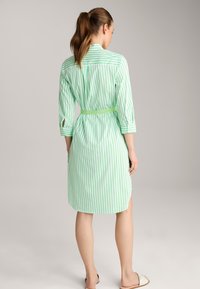 Grün und weiß gestreiftes Hemdkleid mit Taillengurt, Dreiviertelärmeln und seitlichen Schlitzen. Leichter Stoff mit glatter Textur.
