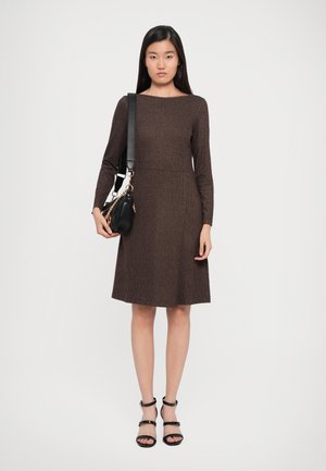Brown, long-sleeve dress with a fitted bodice and flared skirt. Woven texture. Paired with a black handbag and black strappy sandals.