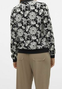 Kwiatowa kurtka bomberka z czarnym tłem i białymi nadrukami peonii, z prążkowanymi mankietami i dołem. Połącz z jasnobeżowymi spodniami.