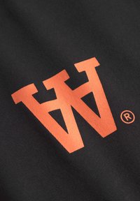 Zwarte stof met een groot, gestileerd oranje logo met scherpe hoeken en een lichte glans, vergezeld van een klein geregistreerd merk symbool.
