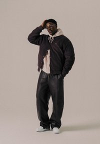 Black corduroy jacket, gray hoodie, black leather pants, and white sneakers. Accessories include glasses and a drawstring on the hoodie.