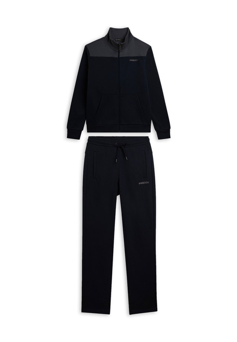 Chándal deportivo azul marino con chaqueta de cremallera que presenta un panel gris y bolsillos, combinado con pantalones a juego con cordón. Textura suave.