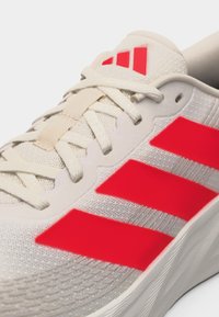 Weißer Sportschuh mit roten Streifen an der Seite und der Zunge, mit weißen Schnürsenkeln und einer Oberseite aus Strickstoff.