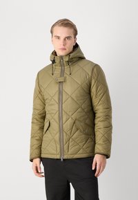 Veste matelassée vert olive avec capuche, présentant des coutures diagonales, une fermeture éclair sur le devant et des poches à pression. Texture douce, design léger.