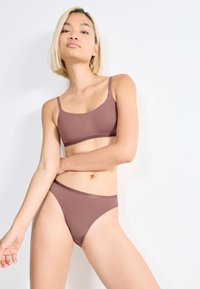 Hnědá bezešvá podprsenka a odpovídající bikiny s tenkými ramínky, hladkým povrchem a minimalistickým designem. Žádné viditelné vzory ani kovové prvky.