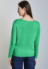 Vihreä pitkähihaine neule, jossa on pyöreä kaula-aukko, valmistettu pehmeästä kankaasta. Sisältää istuvan siluetin sekä ribatut hihansuut ja helman.