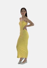 Geel, nauwsluitend jurk met spaghettibandjes, tot halverwege de kuit. Gecombineerd met glanzende zilveren ballerina's, gladde stoftextuur.