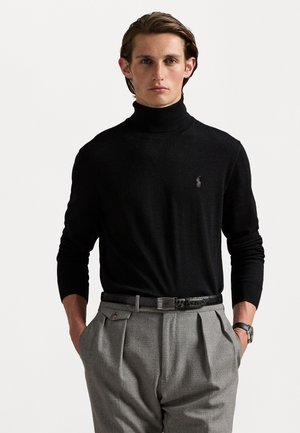 Jersey de cuello alto negro hecho de material de punto, con un logo sutil en el pecho, combinado con pantalones grises y un cinturón negro.