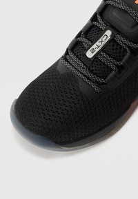 Czarne, oddychające sneakersy z siateczki z szarymi, odblaskowymi sznurowadłami w wzór oraz etykietą "CXT-2" na języku; widoczna krawędź podeszwy na białym tle.