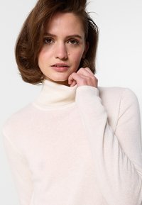 Hellbeige Rollkragenpullover aus weichem, strukturiertem Strick. Figurbetonte Silhouette mit langen Ärmeln und geripptem Kragen. Minimalistisches Design.