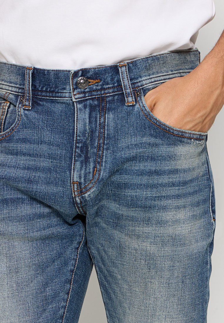 Jeans in denim con un lavaggio blu scuro e aree sbiadite, design a cinque tasche e dettagli di cucitura visibili. Etichetta in pelle sulla cintura.