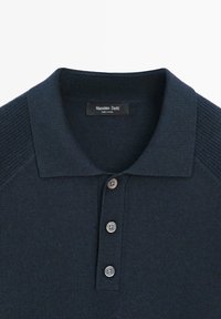 Polo en maille bleu marine foncé avec trois boutons et un col côtelé, avec une étiquette Massimo Dutti à l'intérieur du col.