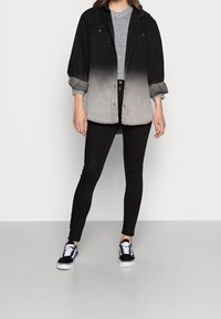 Czarna koszula w dużym rozmiarze z gradientem od czerni do szarości, noszona na szarym swetrze, zestawiona z czarnymi dopasowanymi dżinsami i czarnymi trampkami. Gładka tkanina, casualowy design.