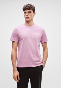 Lys rosa t-skjorte med korte ermer laget av myk bomull, med en liten logo på brystet og en klassisk rund halsutforming.