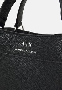 Schwarze Handtasche aus Kunstleder mit strukturierten Oberflächen. Mit einem silbernen A/X-Logo und Akzenten. Besitzt stabile Griffe und metallische Details.