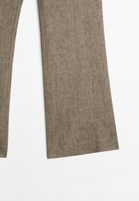 Pantalon en lin marron à larges jambes, posé à plat sur une surface blanche, montrant la texture du tissu et les détails des coutures.