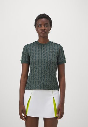 Grünes T-Shirt mit Muster, kurzen Ärmeln, Rundhalsausschnitt und strukturiertem Stoff. Lacoste-Logo auf der linken Brust. Weißer Rock mit neongelben Akzenten.
