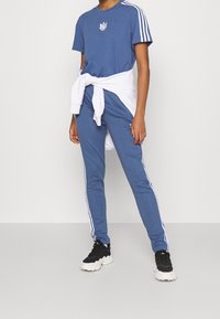 Blått atletiskt outfit bestående av en t-shirt med logotyp, åtsittande byxor med vita sidostråk och svarta sneakers med en kraftig sula.