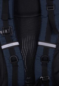 Sac à dos bleu et noir avec bretelles rembourrées, dos en mesh, boucles latérales et accents réfléchissants. Présente une surface texturée et un design robuste.
