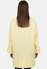 Maglione oversize lavorato a maglia in un morbido giallo, caratterizzato da un motivo testurizzato e ampie maniche risvoltabili. Il tessuto è leggero e traspirante.
