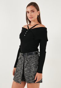 Mlada žena nosi crni top bez ramena s rebrastom teksturom i dugmadi u obliku srca, te crno-bijelu suknju s teksturom i crnim pojasom.