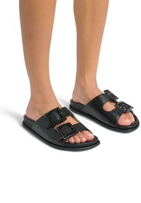 Infradito in pelle nera con due dettagli di fibbia decorativa, texture liscia, design open toe e suola piatta.