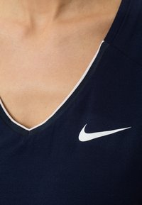 Närbild av ett bröst som bär en marinblå V-ringad tröja med en vit Nike swoosh-logga på högra sidan.
