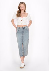 Fehér kötött crop top, rövid ujjakkal, négyzetes nyakkivágással és színes gombos díszítésekkel, világoskék farmer szoknyával párosítva.