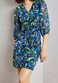 Vestido camisero floral con estampados azules y verdes sobre fondo negro, con mangas de tres cuartos y detalles fruncidos.