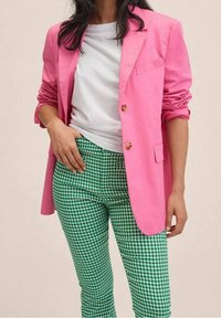 Blazer rose ajusté avec des boutons dorés, associé à un pantalon à motif vichy vert et blanc et un t-shirt blanc, illustrant une tenue décontractée.
