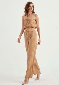 Beżowy, teksturowany zestaw składający się z dwóch części, z strapless topem z marszczeniami oraz luźnymi, wysokimi spodniami.