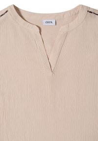 Blouse en tissu texturé beige clair avec un col rond et une petite fente en forme de V à l'avant, étiquetée "CECIL" à l'intérieur du col.