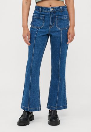 Blå denimflared jeans med kontrastsøm, to frontlommer og høy midje. Stillet med kraftige svarte loafers.