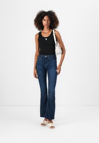 Débardeur noir, jean flared taille haute bleu foncé, sandales blanches avec un accent doré, et un petit sac à main blanc. Design simple et ajusté.