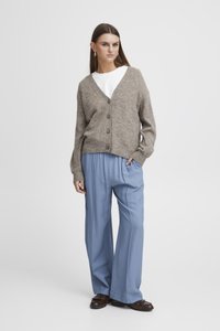Cardigan beige a maglia con scollatura a V e cinque bottoni, abbinato a pantaloni larghi blu chiaro. Mocassini marroni completano l'outfit.