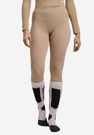 Zbliżenie osoby noszącej beżowe legginsy i beżowe podkolanówki z czarnymi geometrycznymi wzorami, stojącej z nogami złączonymi.