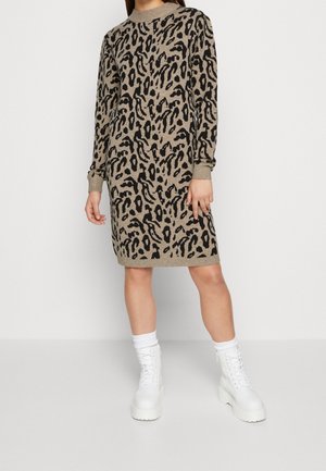 Donna che indossa un abito a maniche lunghe in maglia con stampa leopardata beige e nera, calzini bianchi e stivali bianchi robusti con lacci.