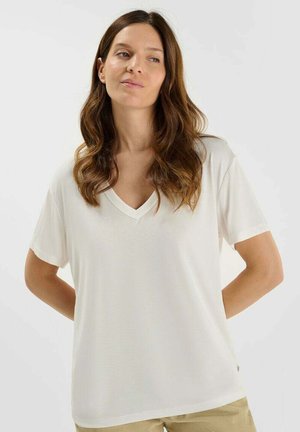 T-shirt blanc à col en V avec des manches courtes, texture lisse, coupe décontractée et peu de détails de couture. Associé à un bas de couleur neutre.