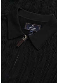 Suéter negro de punto con cuello con cremallera, que presenta un patrón horizontal texturizado. Incluye una etiqueta de tela con el nombre de la marca y detalles de cuidado.