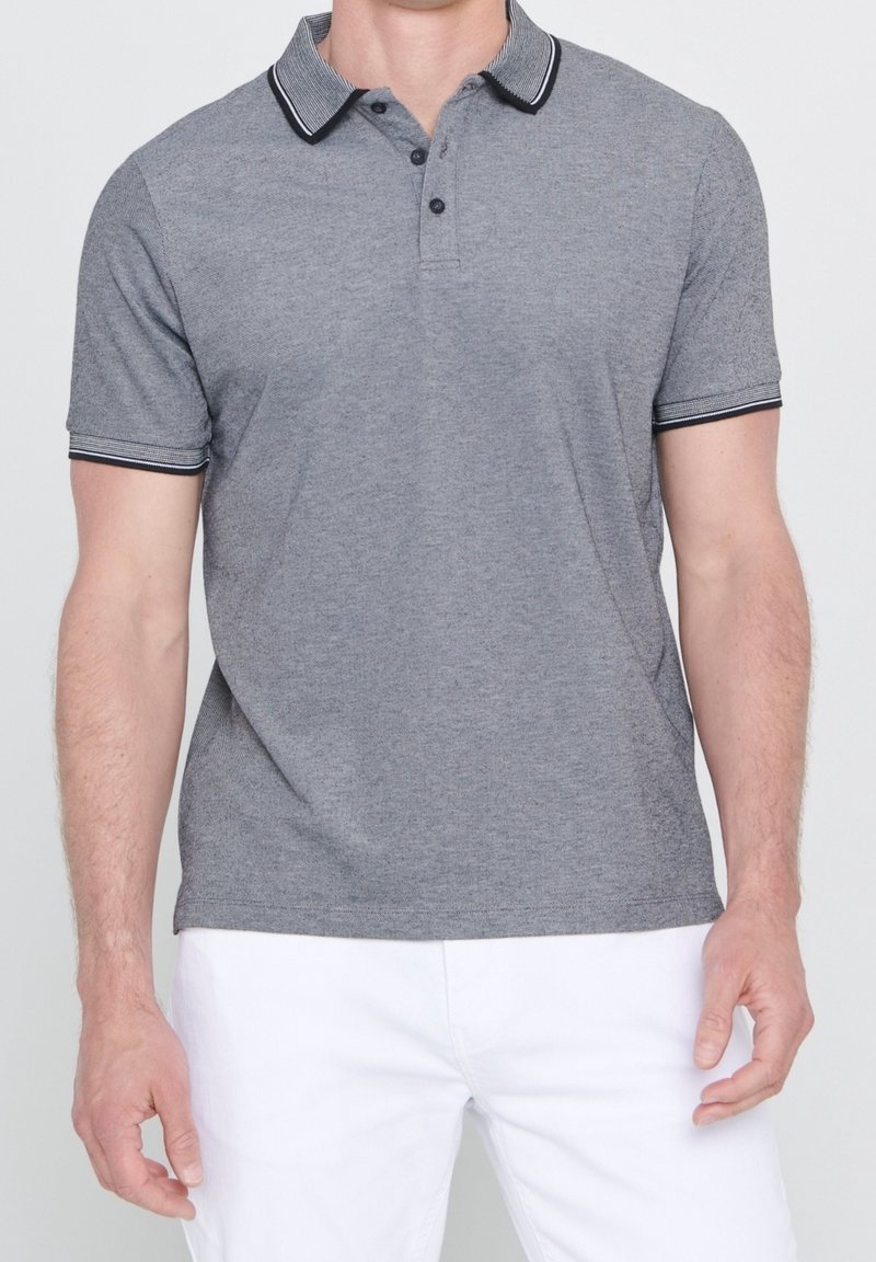 Polo gris con cuello a rayas en blanco y negro, tapeta con tres botones, mangas cortas y textura suave. Se llevan pantalones cortos blancos.