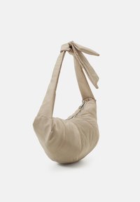 Beige tygväska med en böjd form, dragkedjestängning och ett överdimensionerat knuthandtag. Texturerad yta med synliga sömdetaljer.