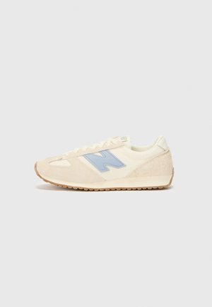 Beige low-top sneaker with light blue "N" logo, textured suede and mesh upper, white laces, and gum rubber sole.