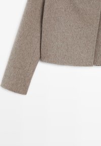Brązowa kurtka z mieszanki wełny z teksturowanym wykończeniem, skróconym krojem i długimi rękawami. Przód ma czysty, otwarty kształt bez zapięć.