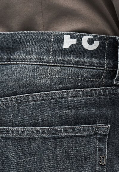 Κοντινή λήψη από τσέπη και ζώνη παντελονιού από σκούρο γκρι τζιν με λευκά τυπωμένα γράμματα και μικρό μεταλλικό γράμμα "D" στην άκρη της τσέπης.