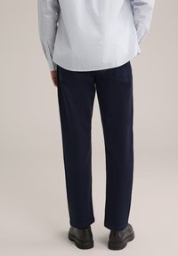 Tamsiai mėlynos kelnės, pagamintos iš tvirto audinio, turinčios tiesią kojos konstrukciją, su užpakalinėmis kišenėmis ir šiek tiek tekstūros. Nešiojamos su šviesiu marškiniu.