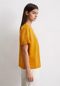 Geel katoenen t-shirt met korte mouwen, in een relaxte fit en met een ronde halslijn. Dit shirt heeft een gladde textuur en zijsplitten voor meer bewegingsvrijheid.
