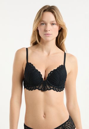 Soutien-gorge en dentelle noire avec un design festonné, doté de bonnets en forme triangulaire et de bretelles réglables. Détails en dentelle texturée sur toute la surface.