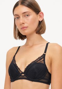 Zwarte kanten bralette met een driehoekige vorm, doorschijnende stof, ingewikkelde bloemmotieven, verstelbare bandjes en een uitsnijding aan de voorkant.